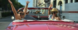 Two people in a red car waving to the camera.