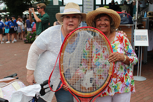 Two women holding a tennis racket in front of them.