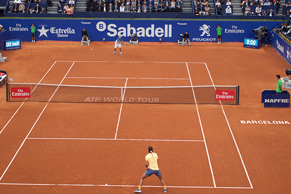Two men playing tennis on a clay court.