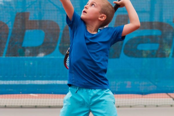 A young boy is playing tennis on the court.