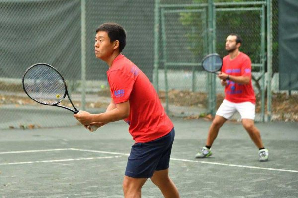 Two men playing tennis on a court with one holding his racket.