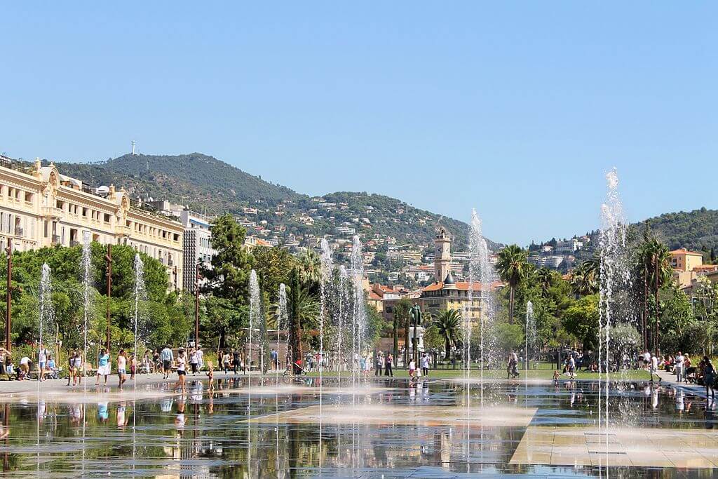 A fountain in the middle of a park with people walking around.