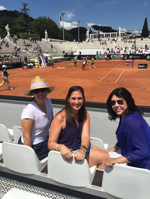 Three women sitting in a row on the tennis court.