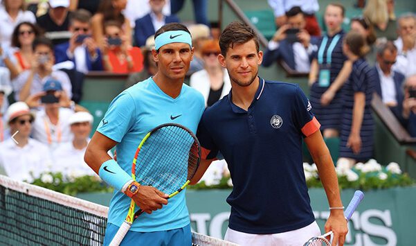 Two men standing next to each other holding tennis rackets.