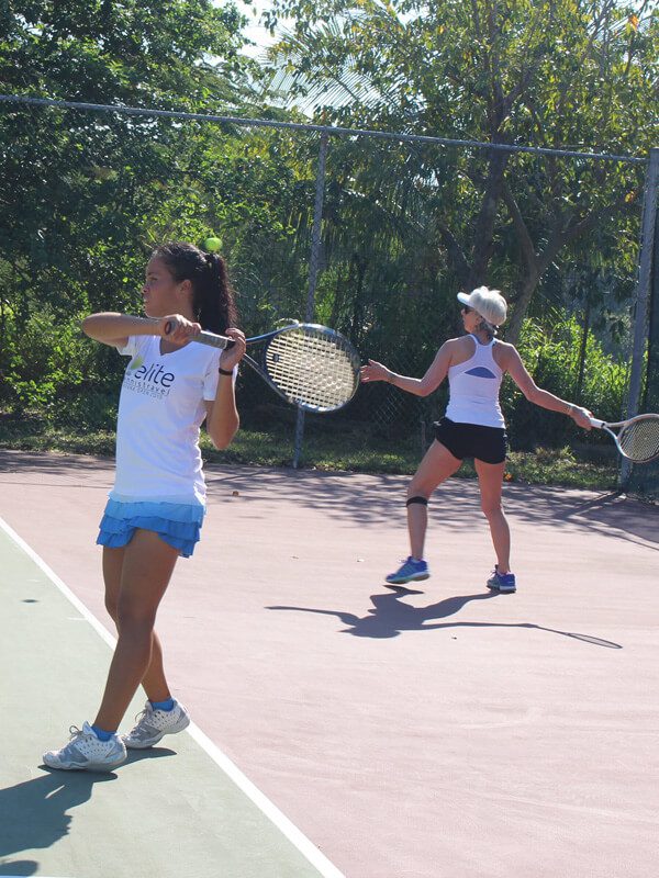 Two women playing tennis on a court with trees in the background.