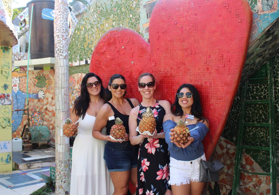 Four women holding pineapples in front of a giant heart.